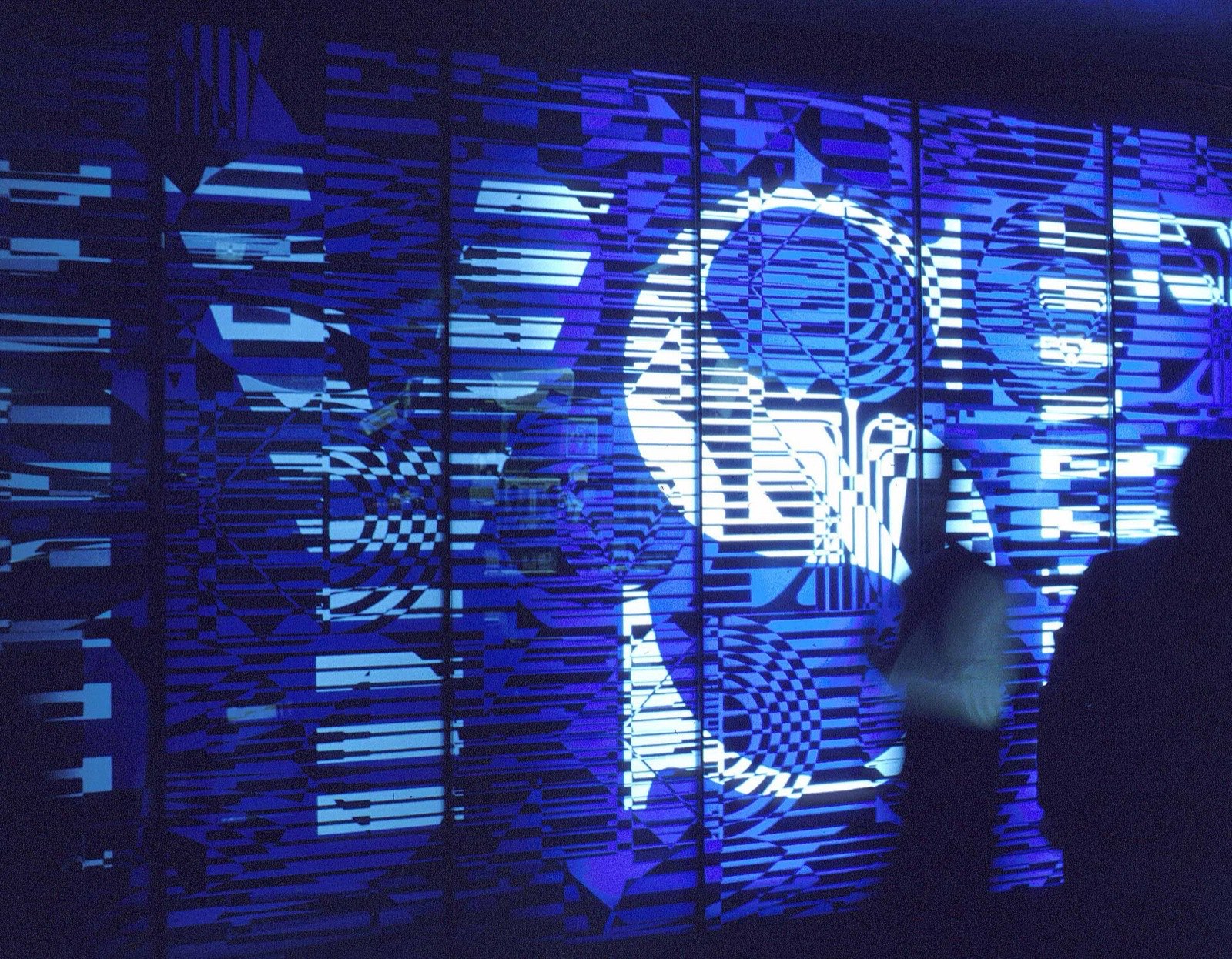 A wall of trading screens on the floor of the New York Stock Exchange, two traders in silhouette